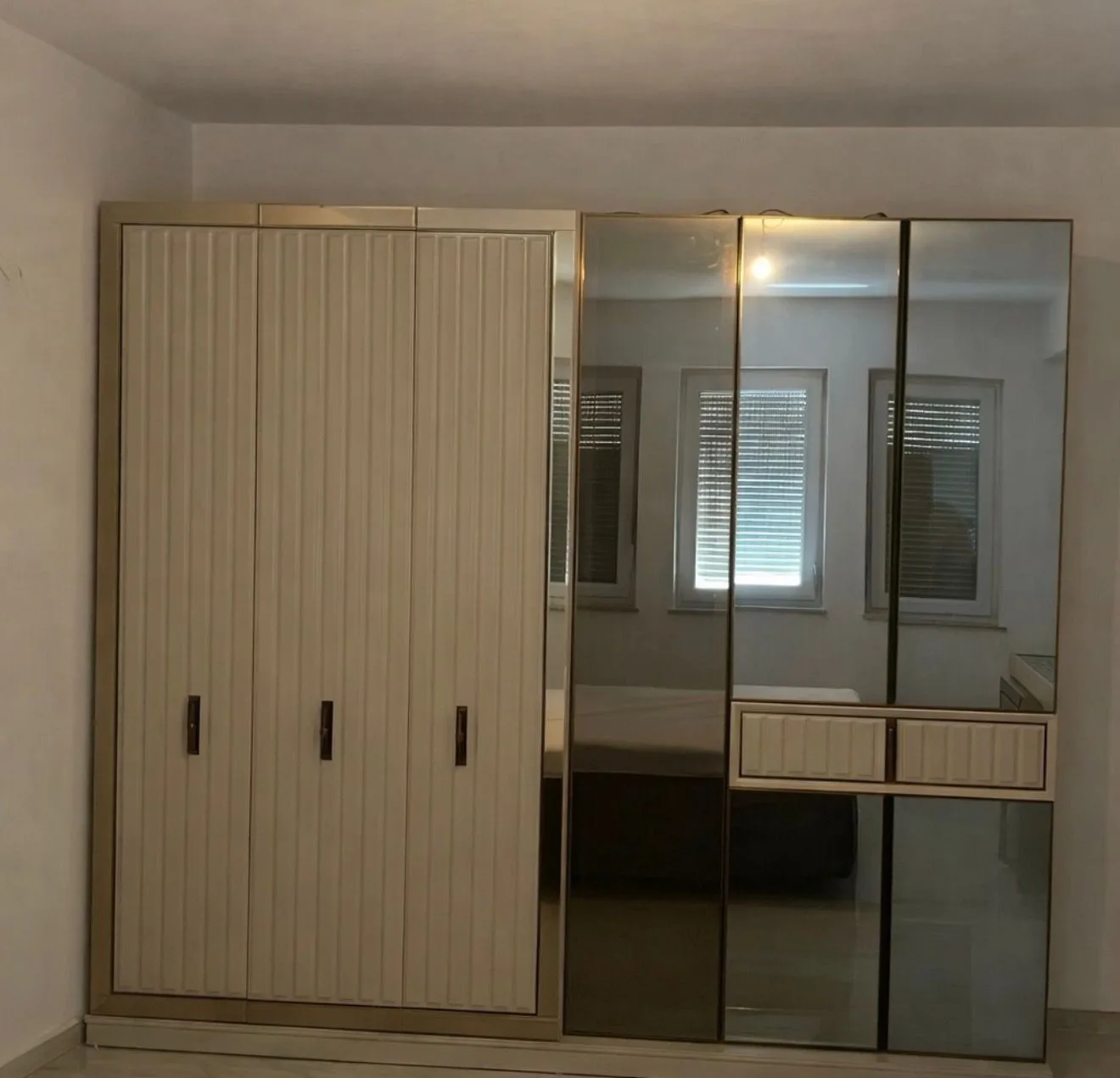 Armoire de chambre à six portes, trois blanc cassé cannelées avec poignées sombres et trois en verre miroir fumé encadrant deux tiroirs cannelés