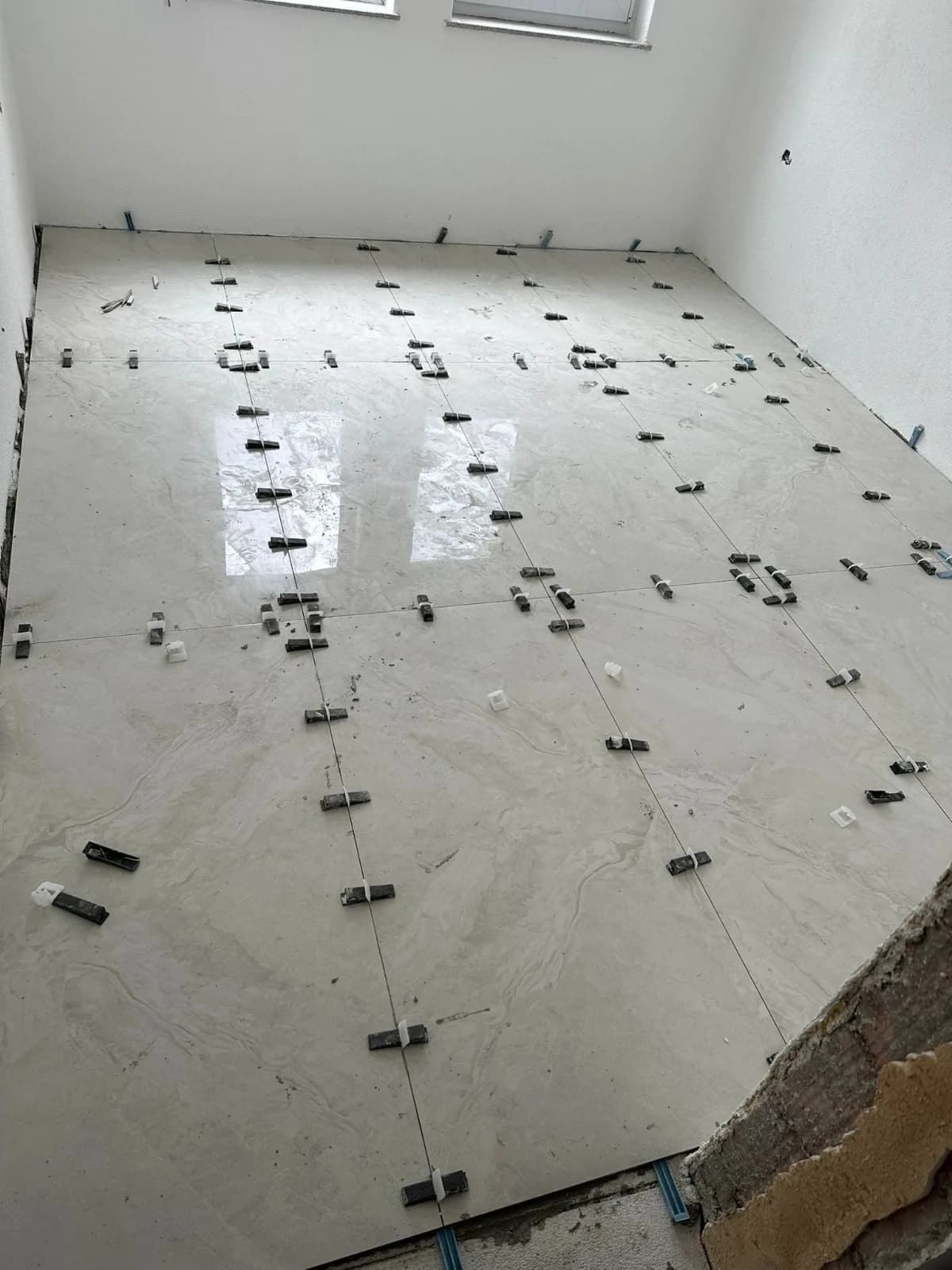 Pose en cours de grands carreaux gris clair effet marbre, les cales de nivellement noires encore en place à chaque joint